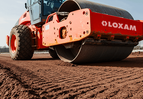 Equipamento para construção civil: um compactador de solo da marca Loxam sendo utilizado na fase de terraplanagem de uma obra para garantir uma base firme.