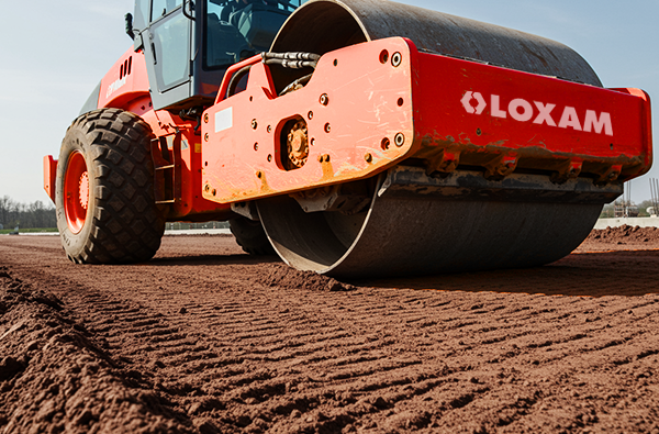 Equipamento para construção civil: um compactador de solo da marca Loxam sendo utilizado na fase de terraplanagem de uma obra para garantir uma base firme.